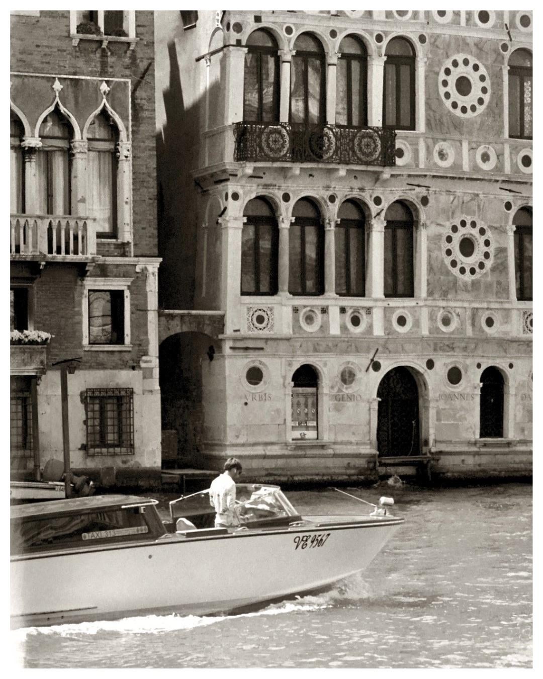 A man drives a boat past ornate buildings in Venice.
