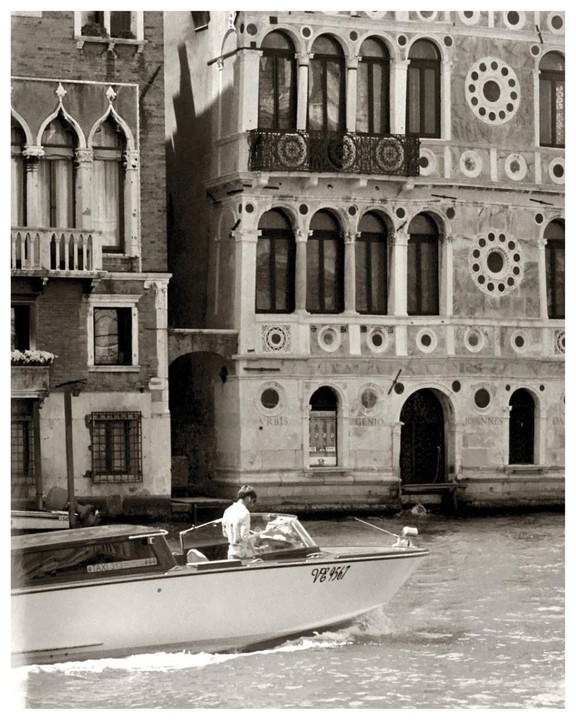 A man drives a boat past ornate buildings in Venice.