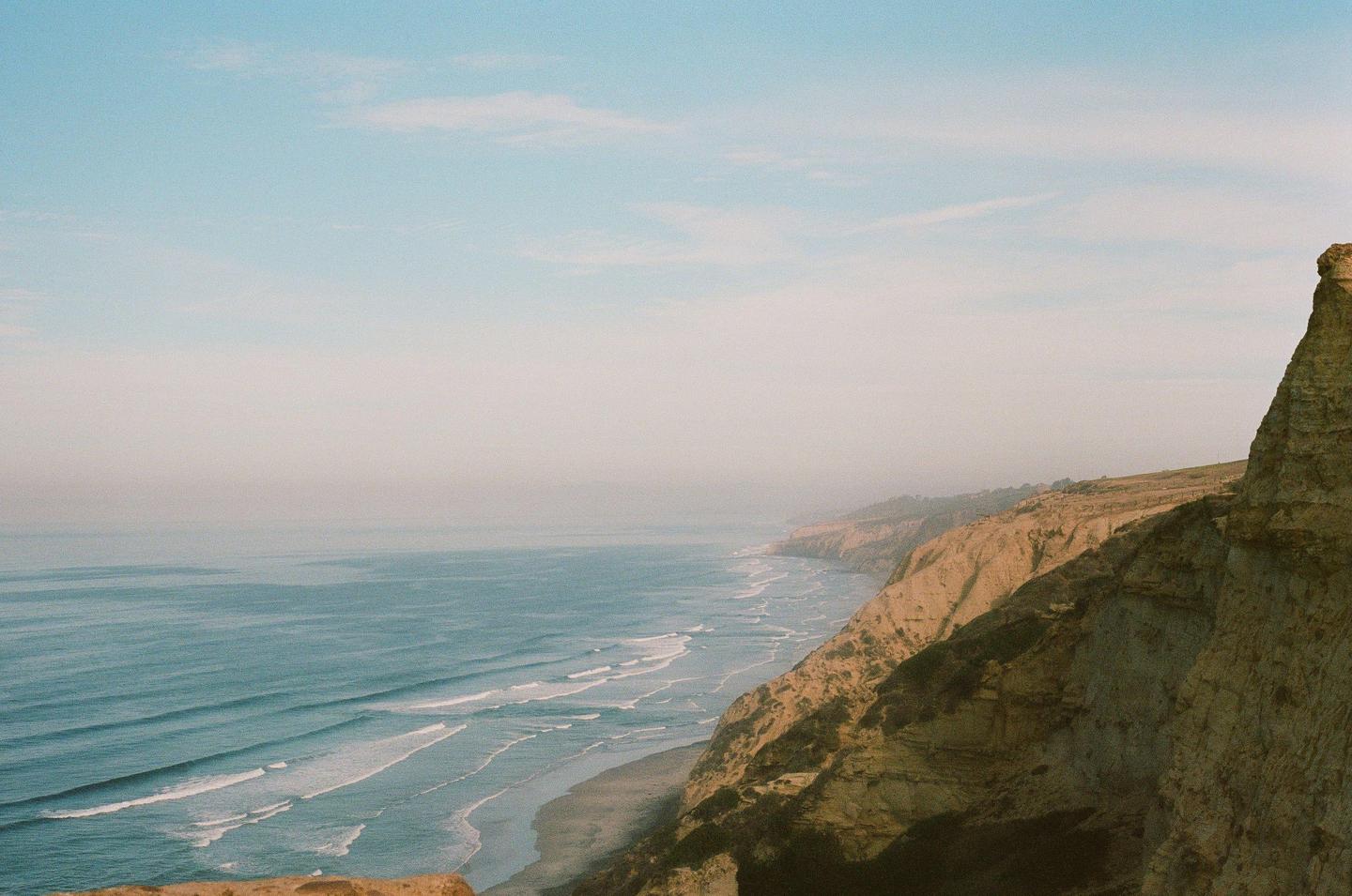 A hazy coastline with cliffs and waves breaking on the shore is visible under a light blue sky.