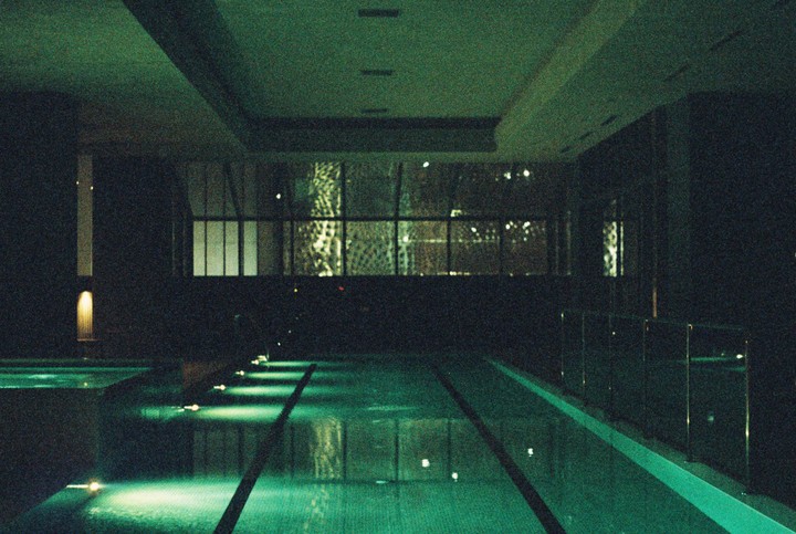 A dark indoor swimming pool is illuminated by green lights reflecting on the water.