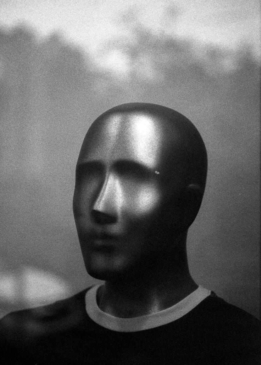 A mannequin head with a shiny surface is shown in profile, wearing a shirt with a white collar.