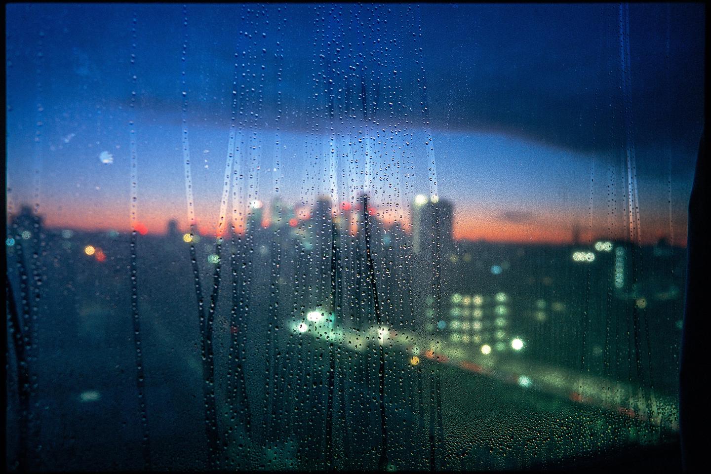 Raindrops cover a window looking out at a city skyline at dusk.