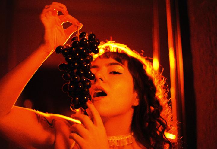 A woman holds a bunch of grapes to her mouth, illuminated by orange light.