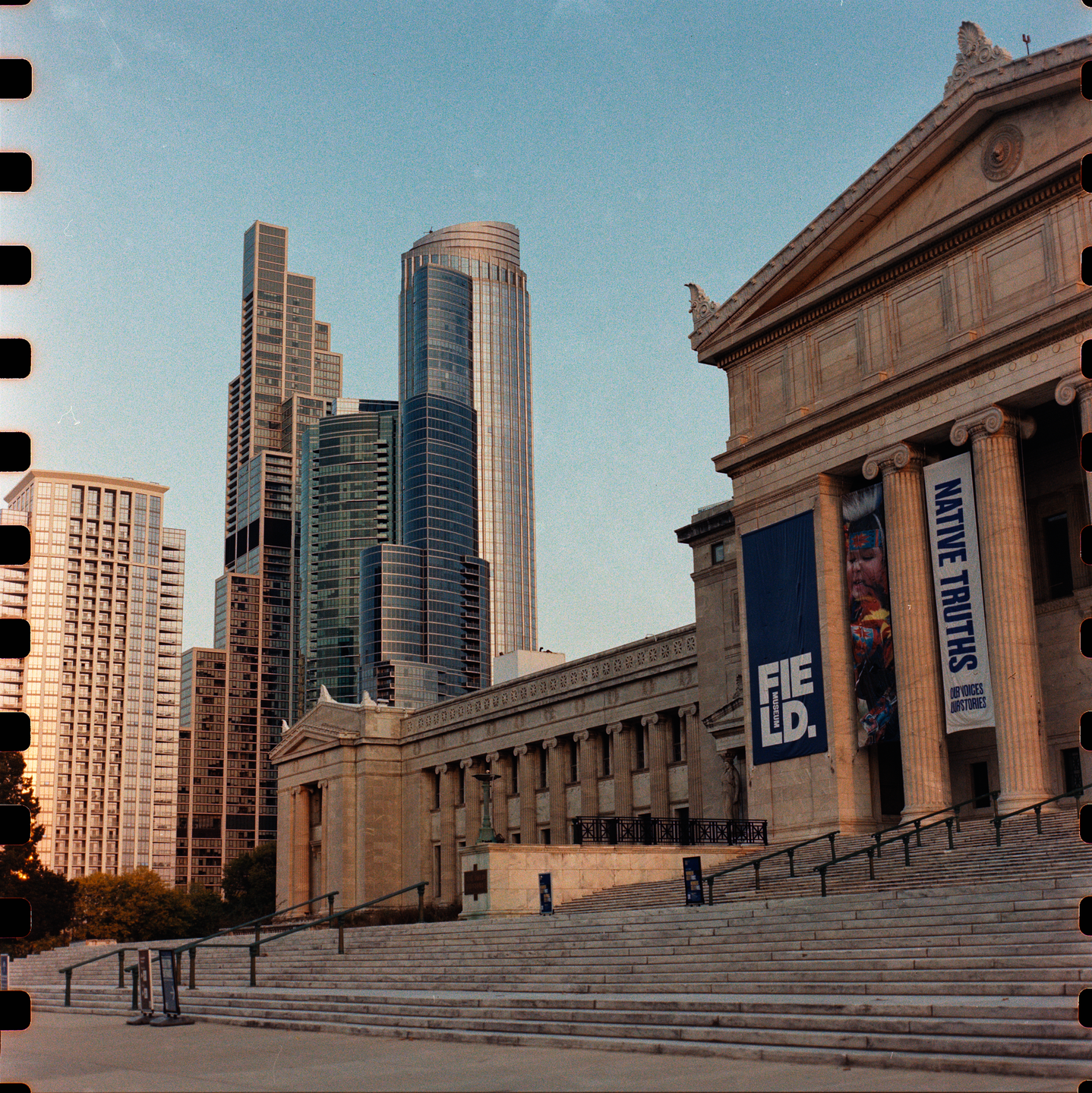 A grand museum building with large steps and banners stands in front of modern skyscrapers under a clear sky.