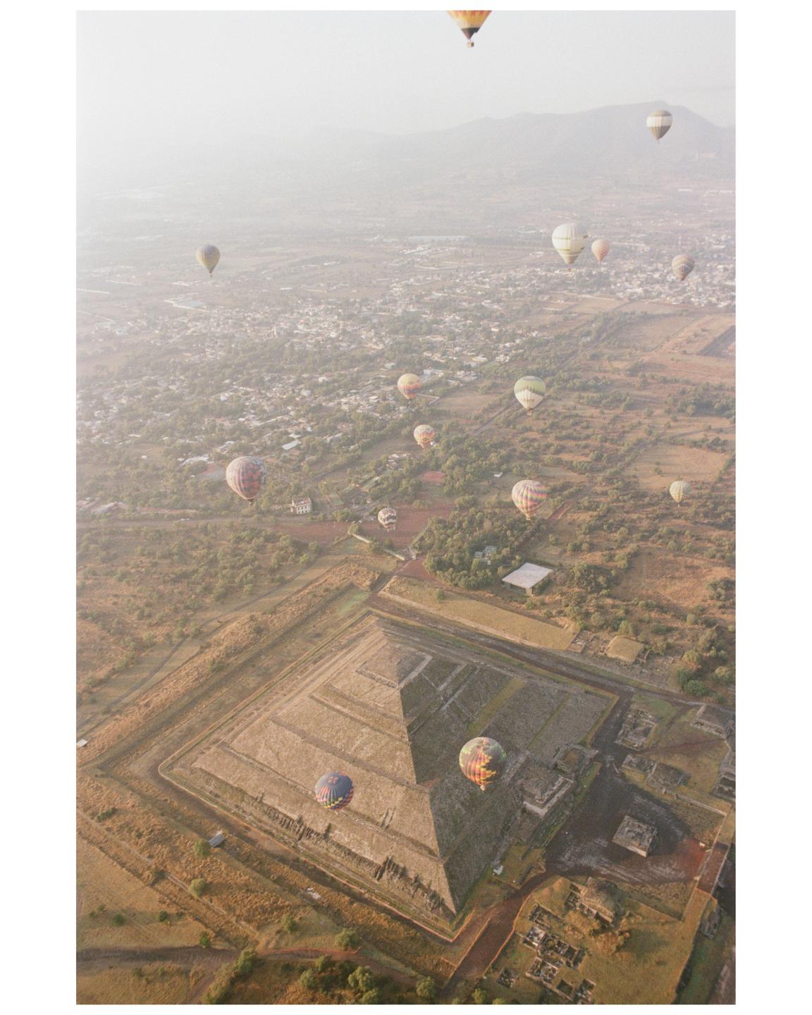 Hot air balloons float above the ancient Teotihuacan pyramids and surrounding landscape.