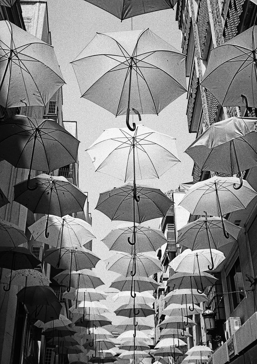 Many umbrellas are suspended above a street between buildings.