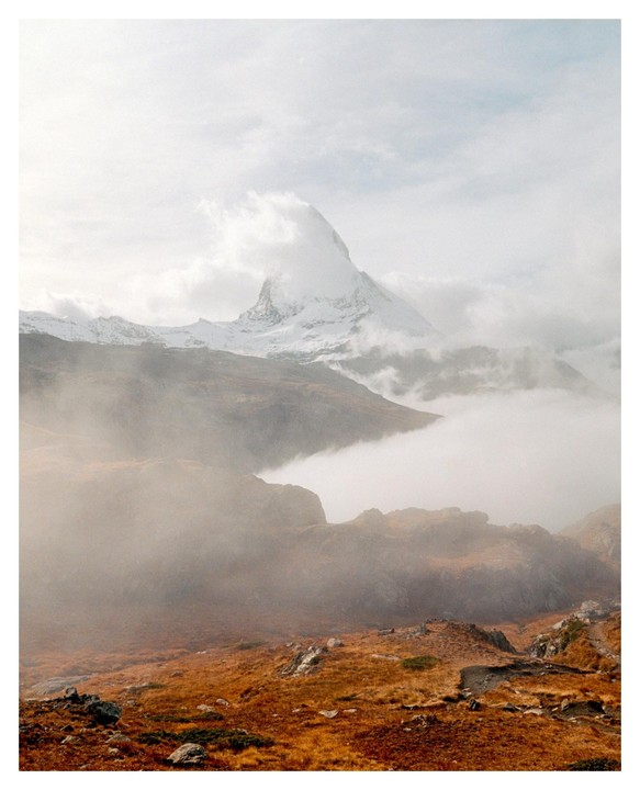 A snow-capped mountain peak rises above a valley filled with fog and autumn foliage.