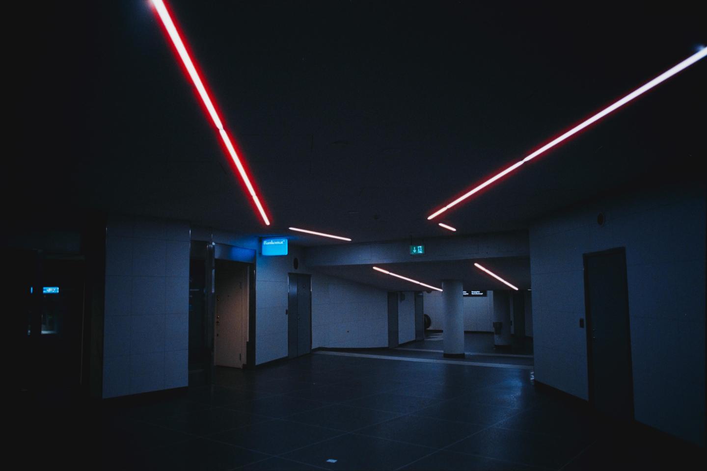 Red neon lights illuminate a dark subway station.