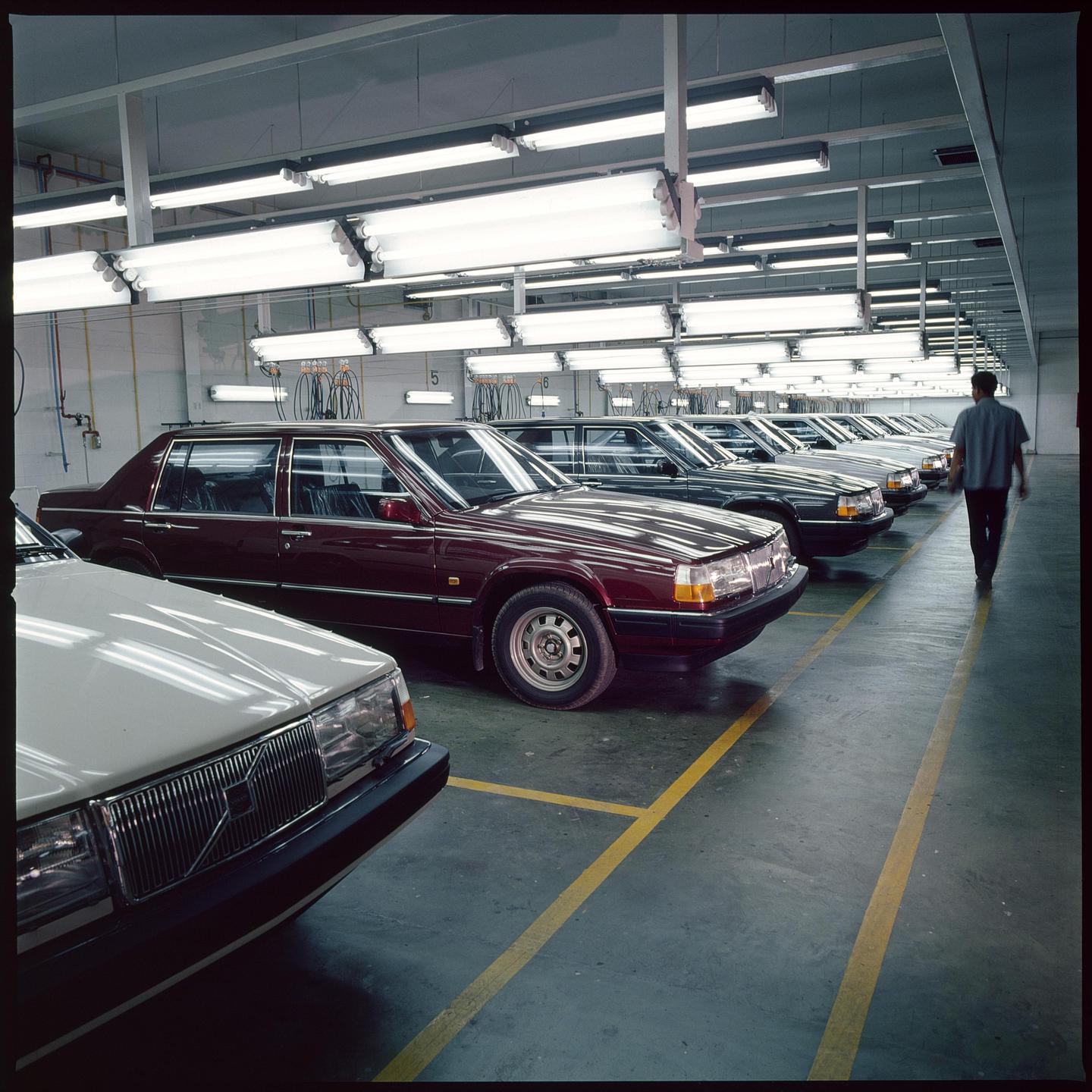 A man walks past a row of cars in a brightly lit garage.