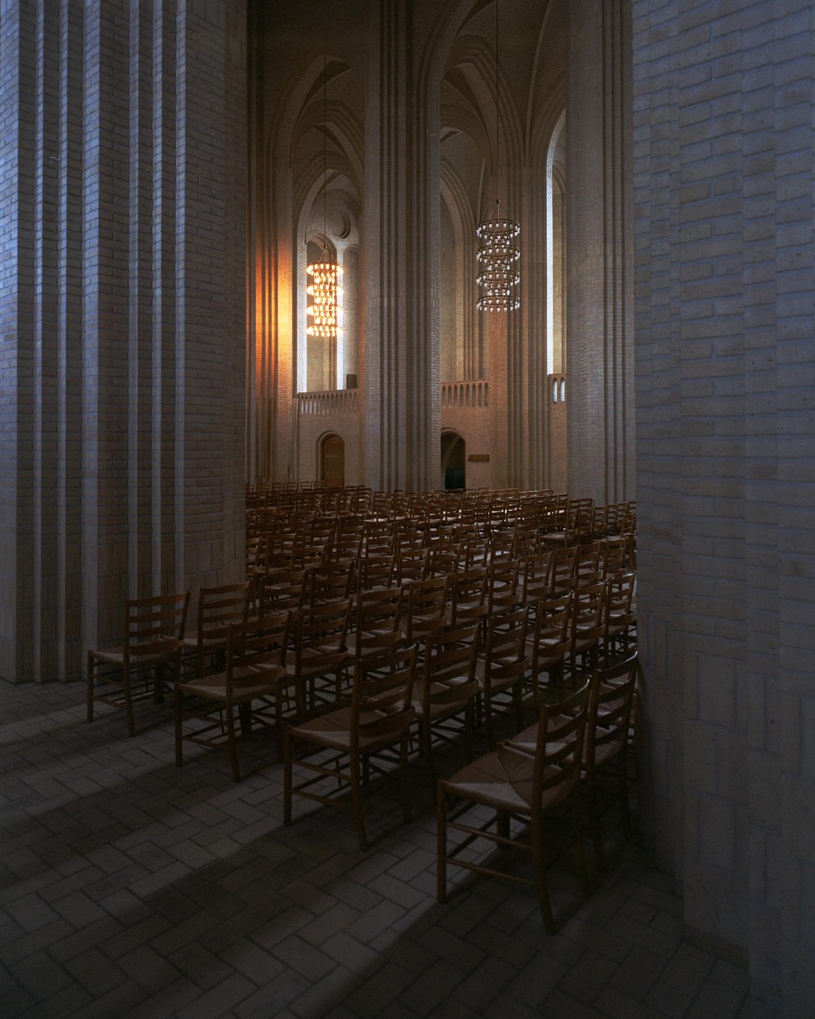 Rows of wooden chairs face an altar in a large church with tall brick columns and chandeliers.