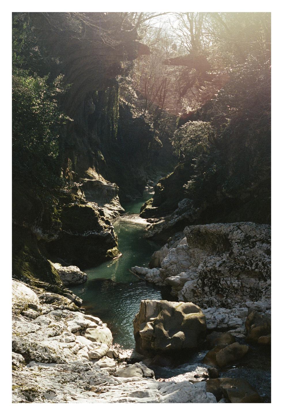 A river flows through a rocky canyon with lush green foliage on the banks.
