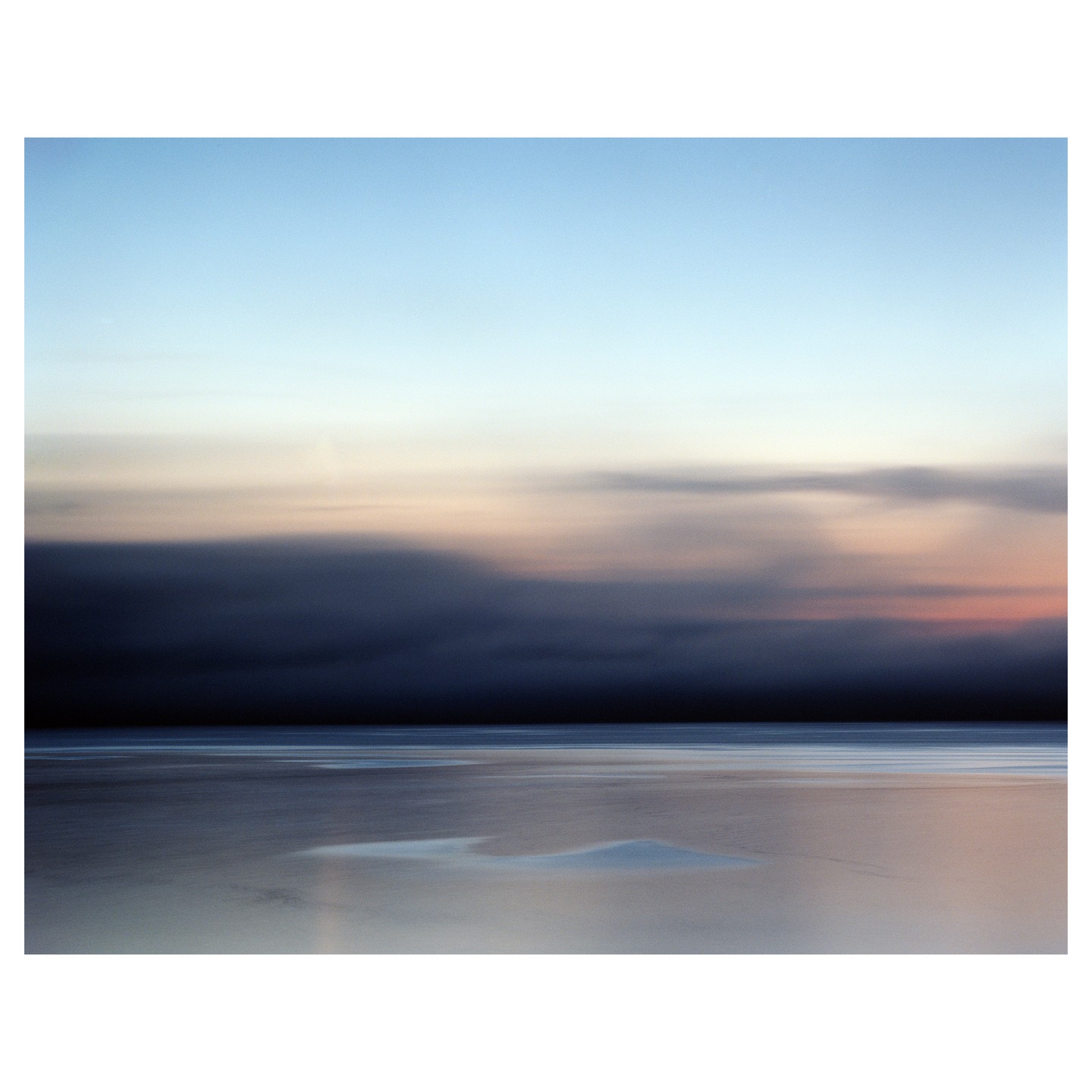 A long exposure photograph captures a dark storm cloud approaching over a calm body of water with a light sky above.