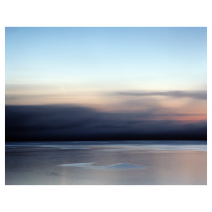 A long exposure photograph captures a dark storm cloud approaching over a calm body of water with a light sky above.
