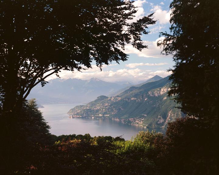 A large lake is surrounded by mountains and trees under a cloudy sky.