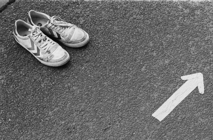 A pair of worn sneakers rests on asphalt next to a painted arrow pointing right.
