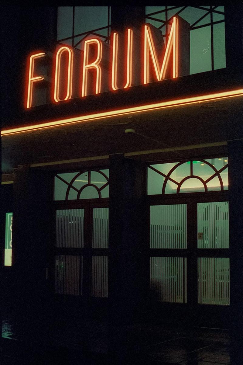 The neon sign for "FORUM" glows above the entrance to a building at night.