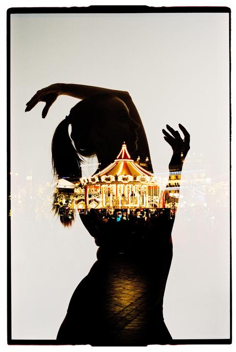 A double exposure shows the silhouette of a woman overlaid with a brightly lit carousel at night.