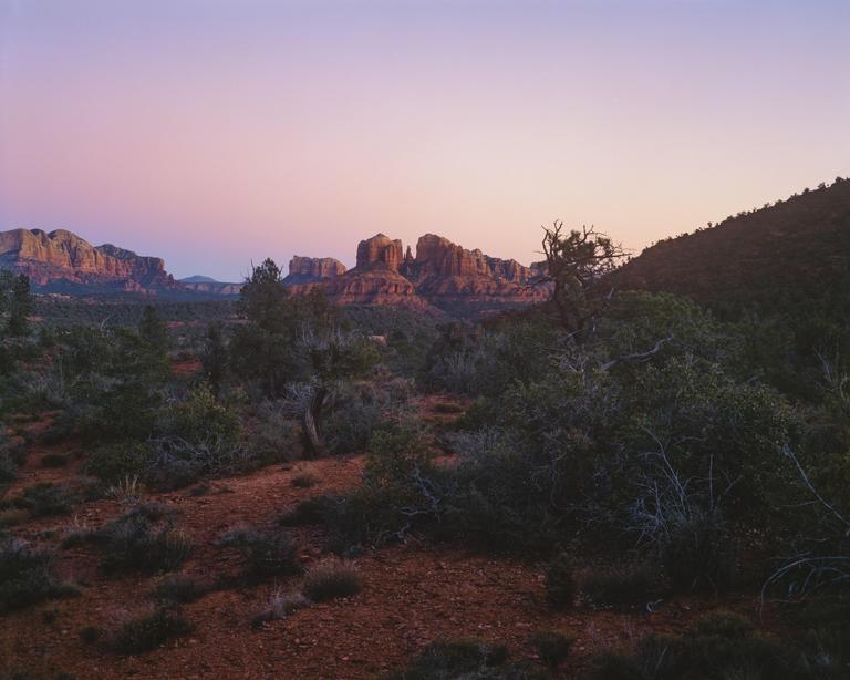 A desert landscape with red rock formations in the distance is visible under a colorful sky.