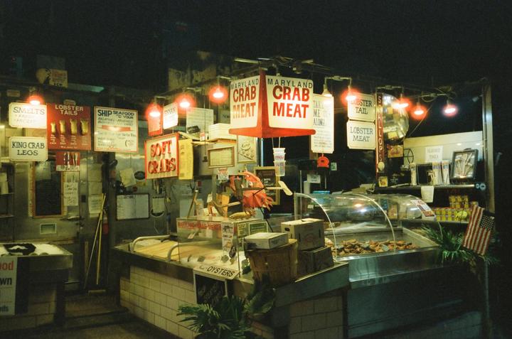 A seafood market at night is illuminated by red lights and signs advertising crab meat, lobster, and oysters.