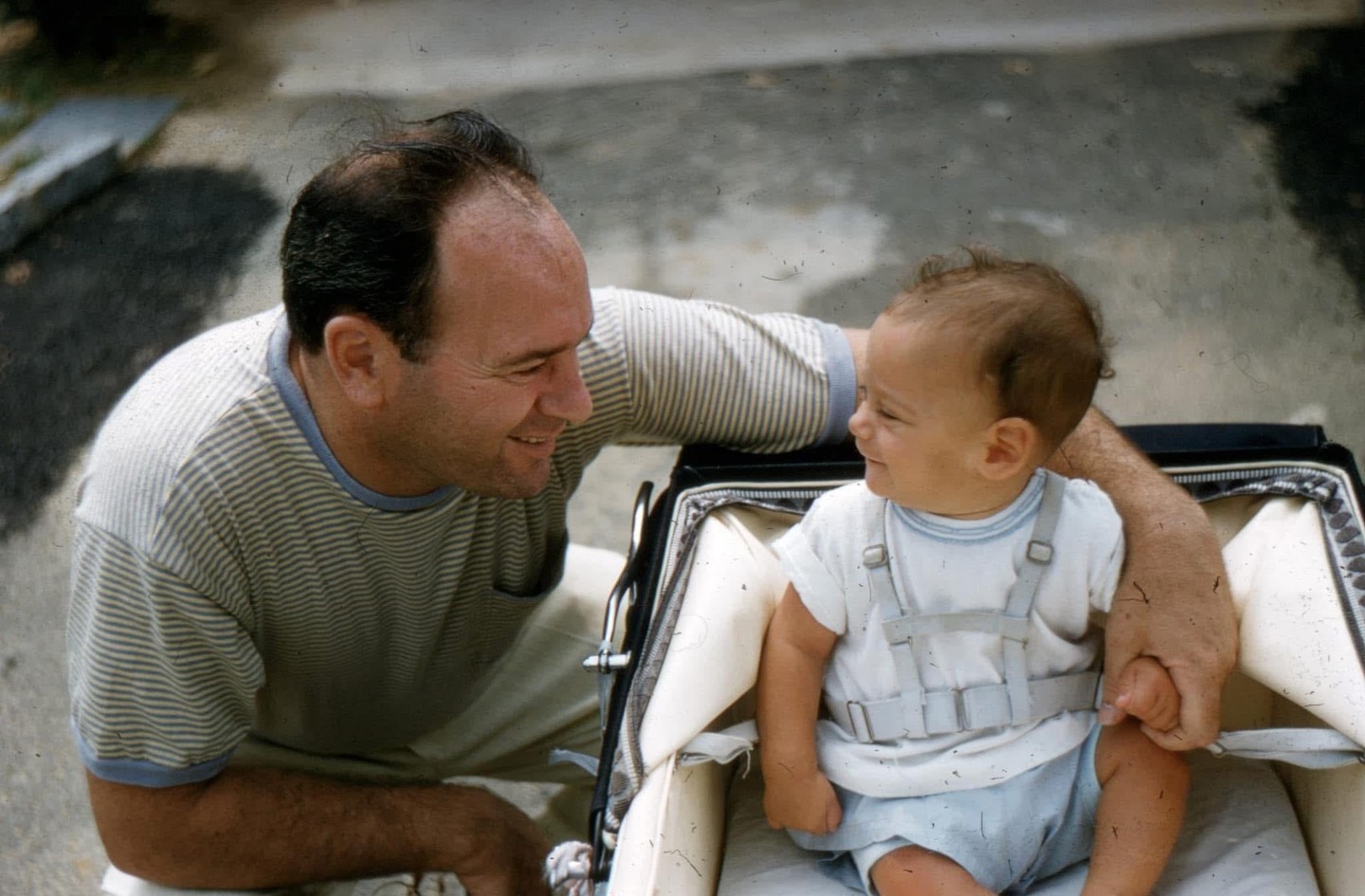 A man smiles at a baby sitting in a stroller.