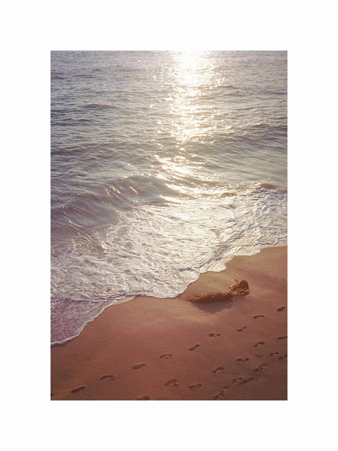 The sun reflects on the ocean waves as they meet the sandy beach with footprints.