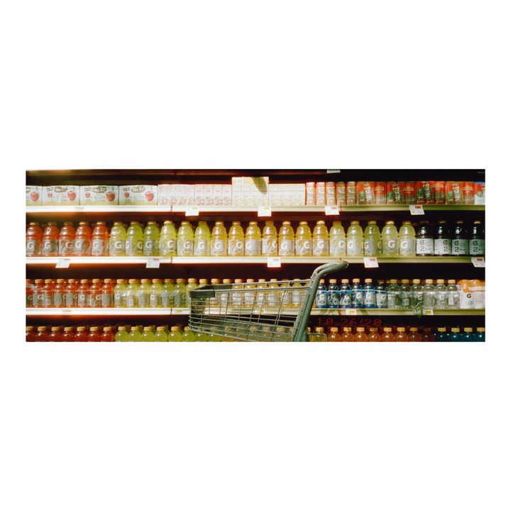 A shopping cart is visible in an aisle filled with bottles of sports drink.