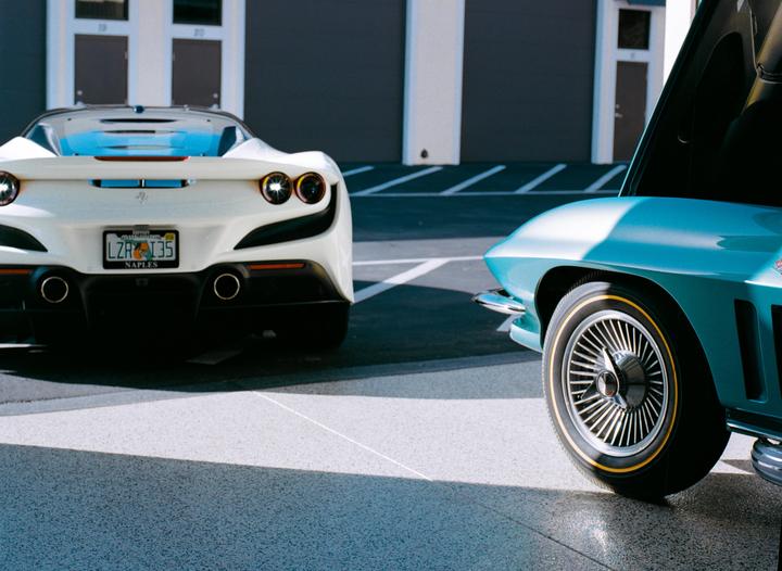 A white sports car is parked next to a blue sports car with its hood open.