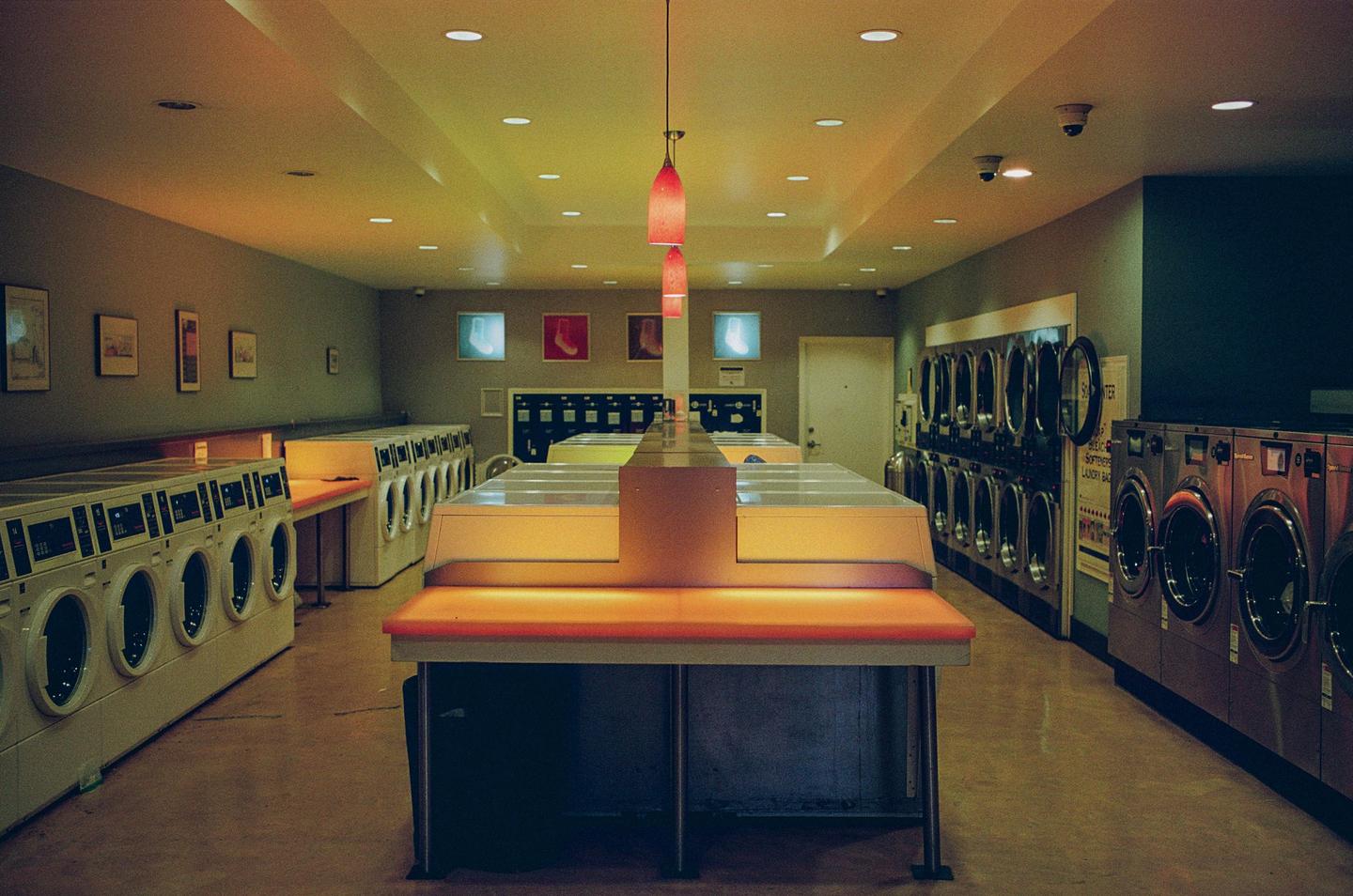 A long, empty laundromat is lit by warm, colorful lights.