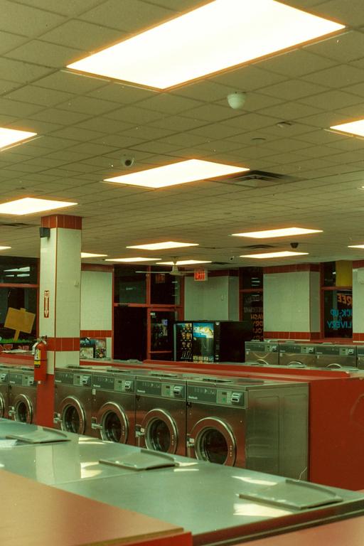 A row of washing machines and folding tables are visible in a brightly lit laundromat.