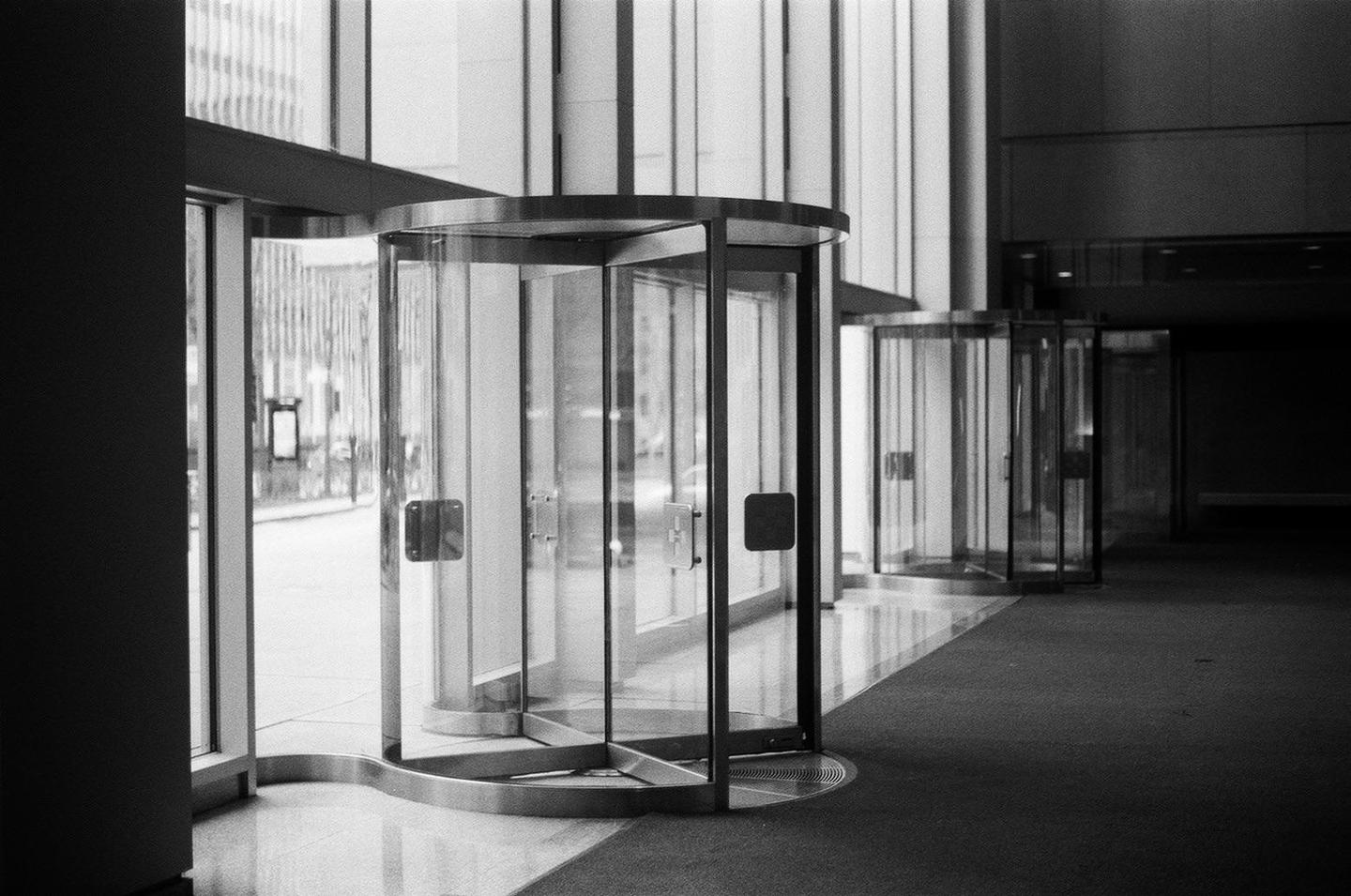 Three revolving doors are visible in a modern building with a dark carpeted floor and reflective tiled floor.