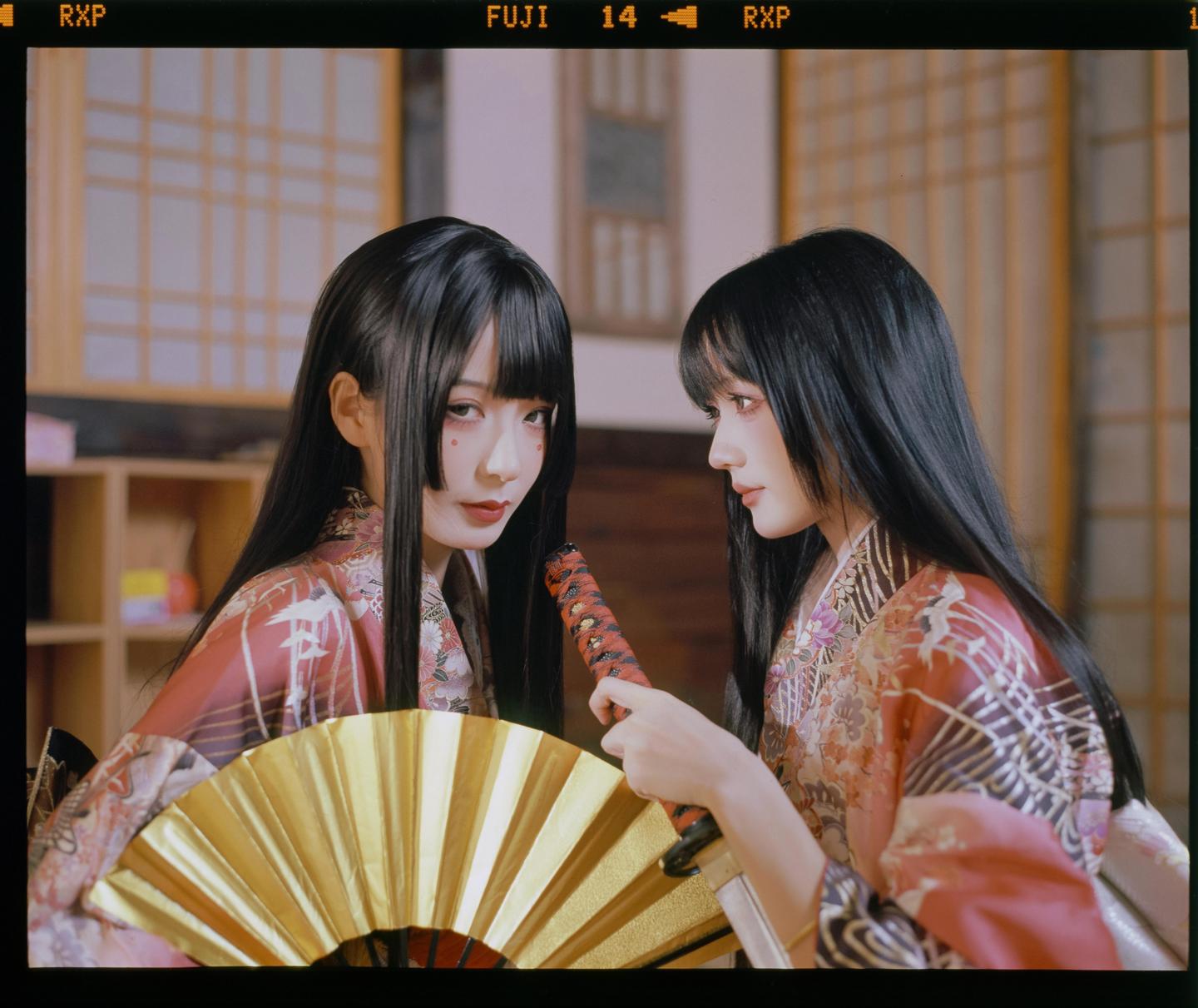 Two women in kimonos are posing with a fan and a sword.