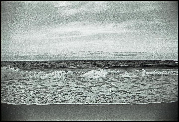 Waves crash onto a sandy beach under a cloudy sky.