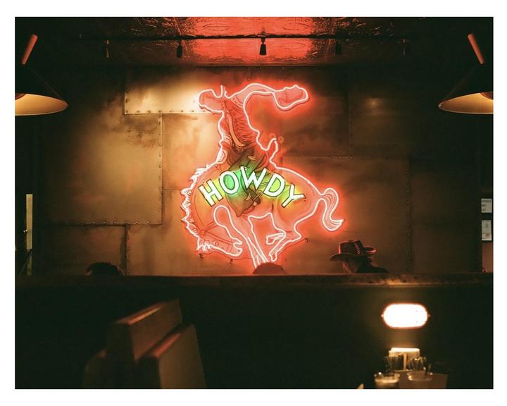 A neon sign depicting a cowboy riding a horse with the word "HOWDY" is illuminated in a dimly lit interior.