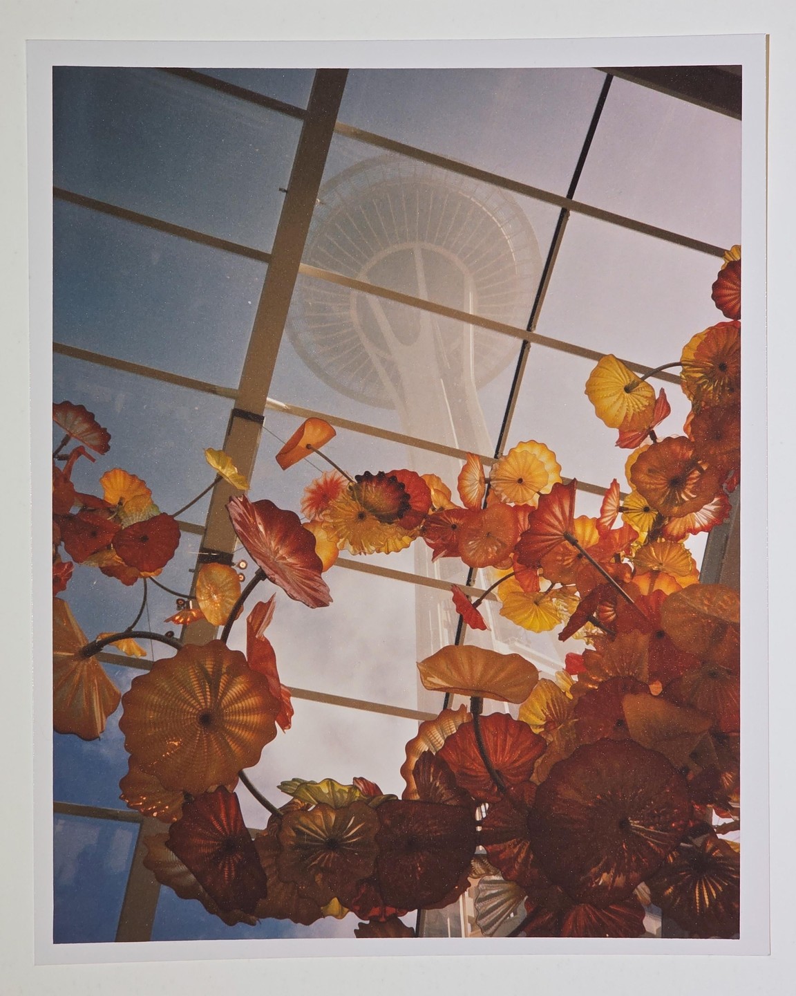 The Space Needle is visible through a glass ceiling adorned with colorful glass sculptures.