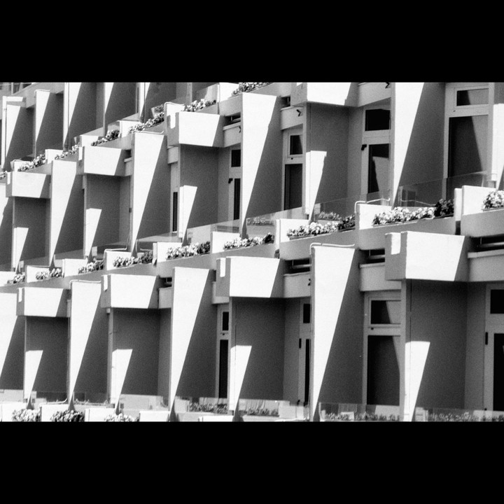 A repeating pattern of balconies with planters is visible on the side of a building.