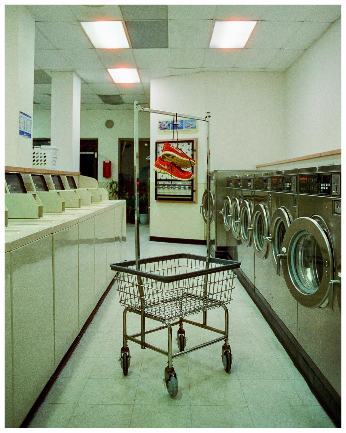 A pair of red sneakers hangs from a laundry cart in a laundromat.
