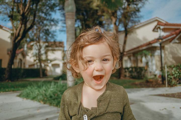 A child with curly hair and an open mouth looks directly at the viewer.