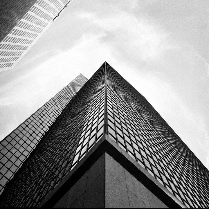 Two tall buildings with many windows are seen from below, with one building's corner pointing towards the sky.