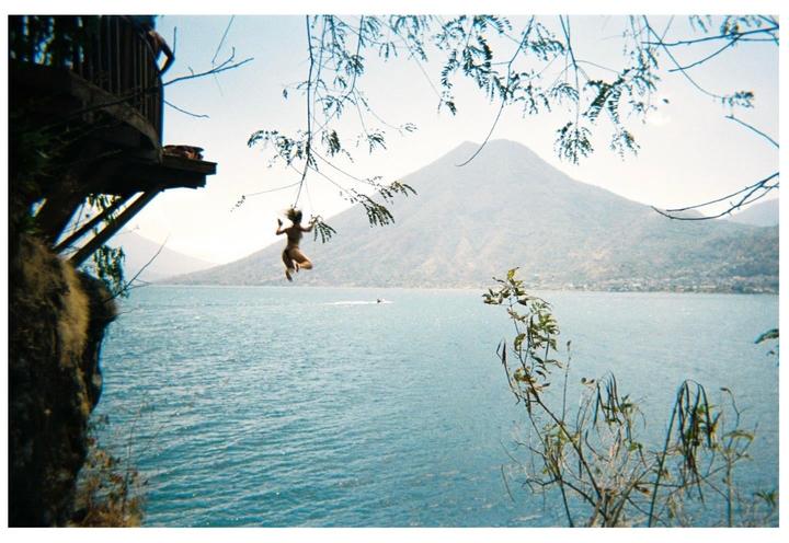 A woman swings from a rope over a lake with mountains in the background.