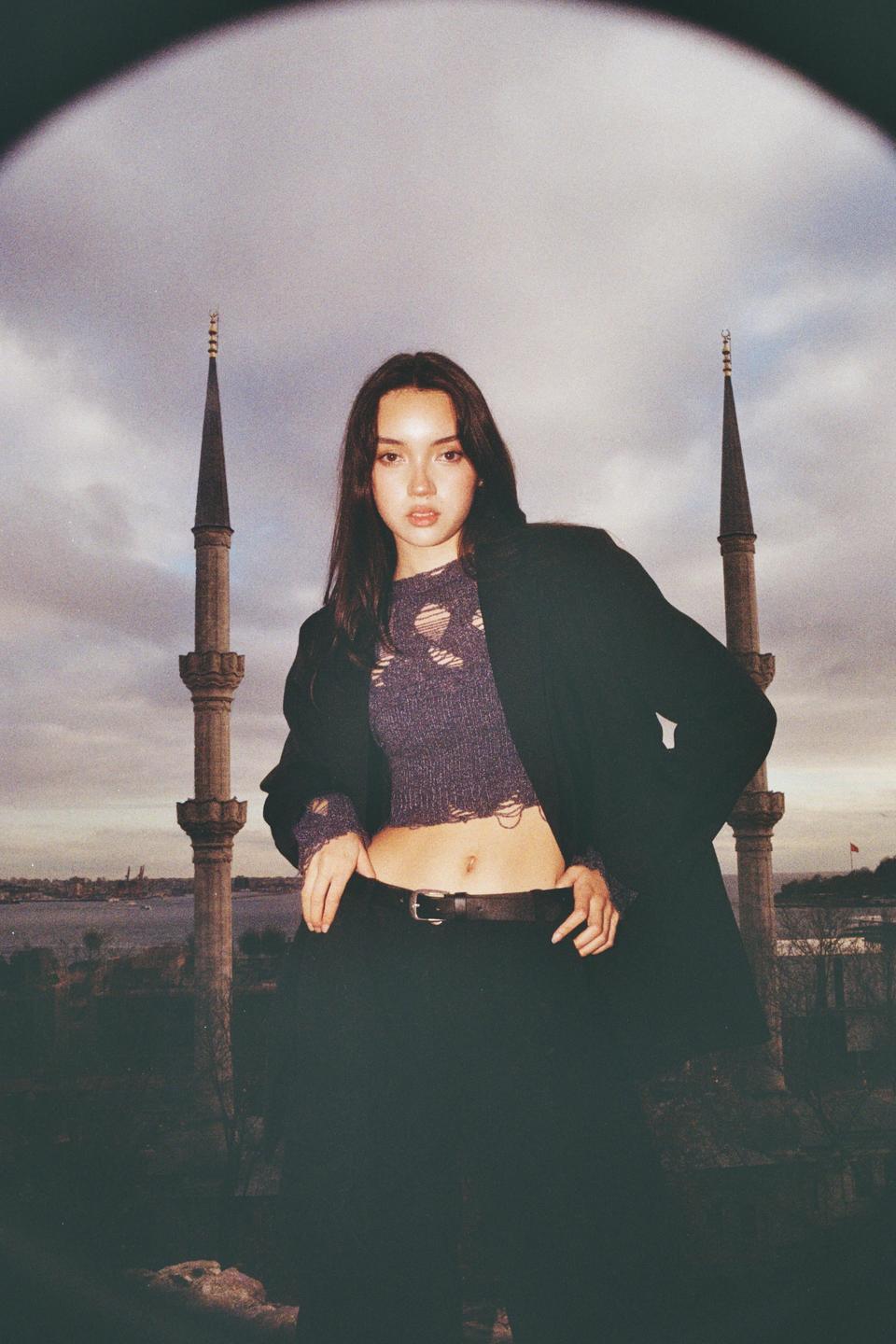 A woman stands in front of two minarets under a cloudy sky.