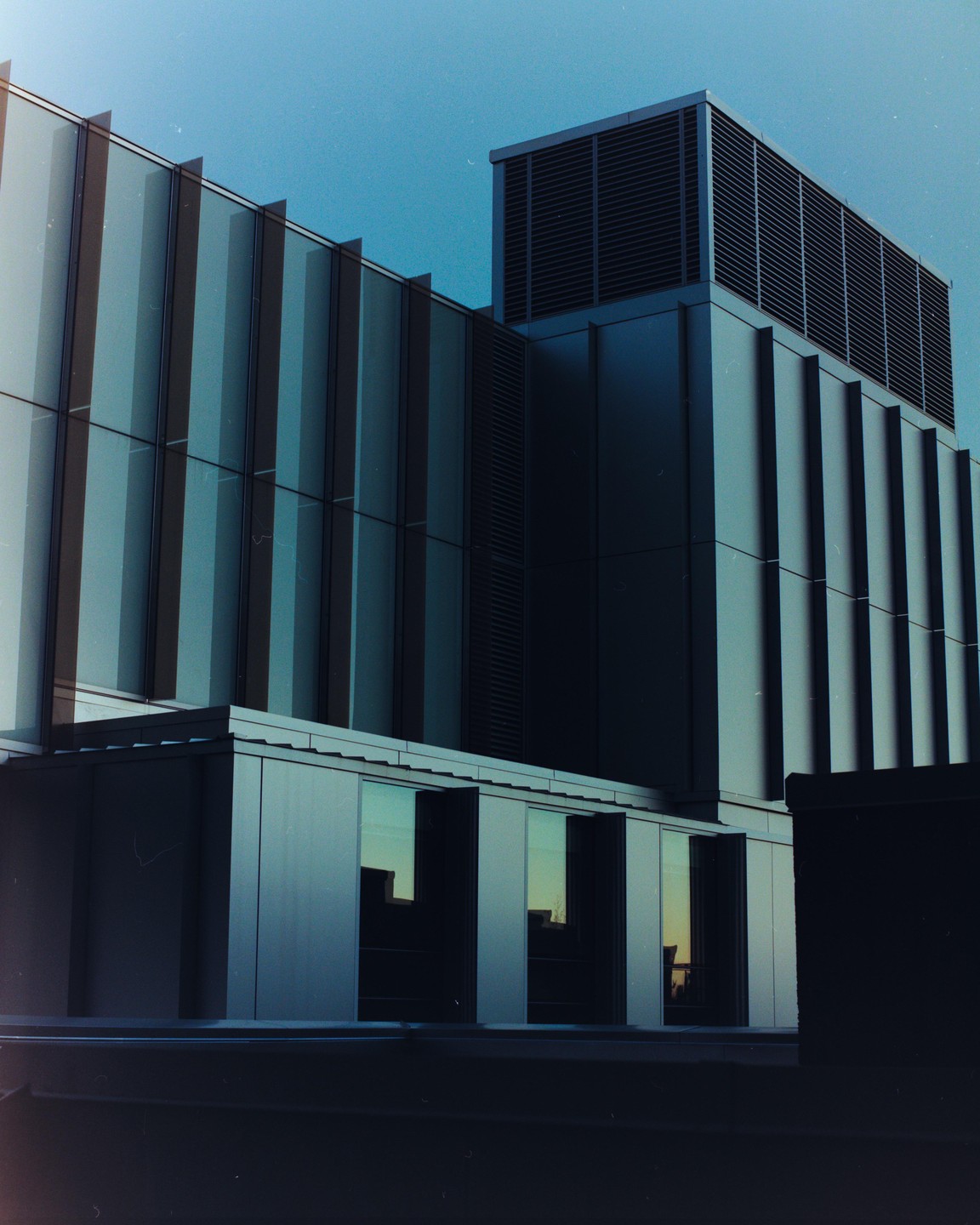 A modern building with glass and metal facades stands against a clear sky.