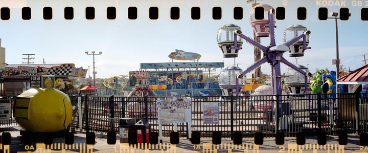 An amusement park with various rides, including a Ferris wheel and roller coaster, is visible behind a black fence.