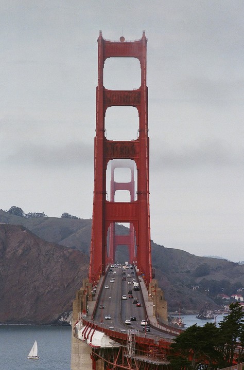The Golden Gate Bridge is visible from a distance, with a sailboat on the water and cars on the bridge.