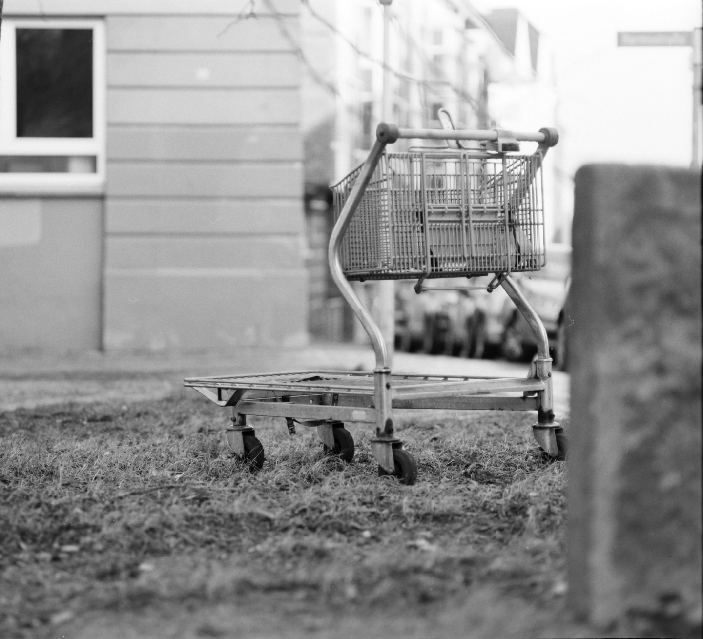 A shopping cart sits on a patch of grass next to a building with a window.