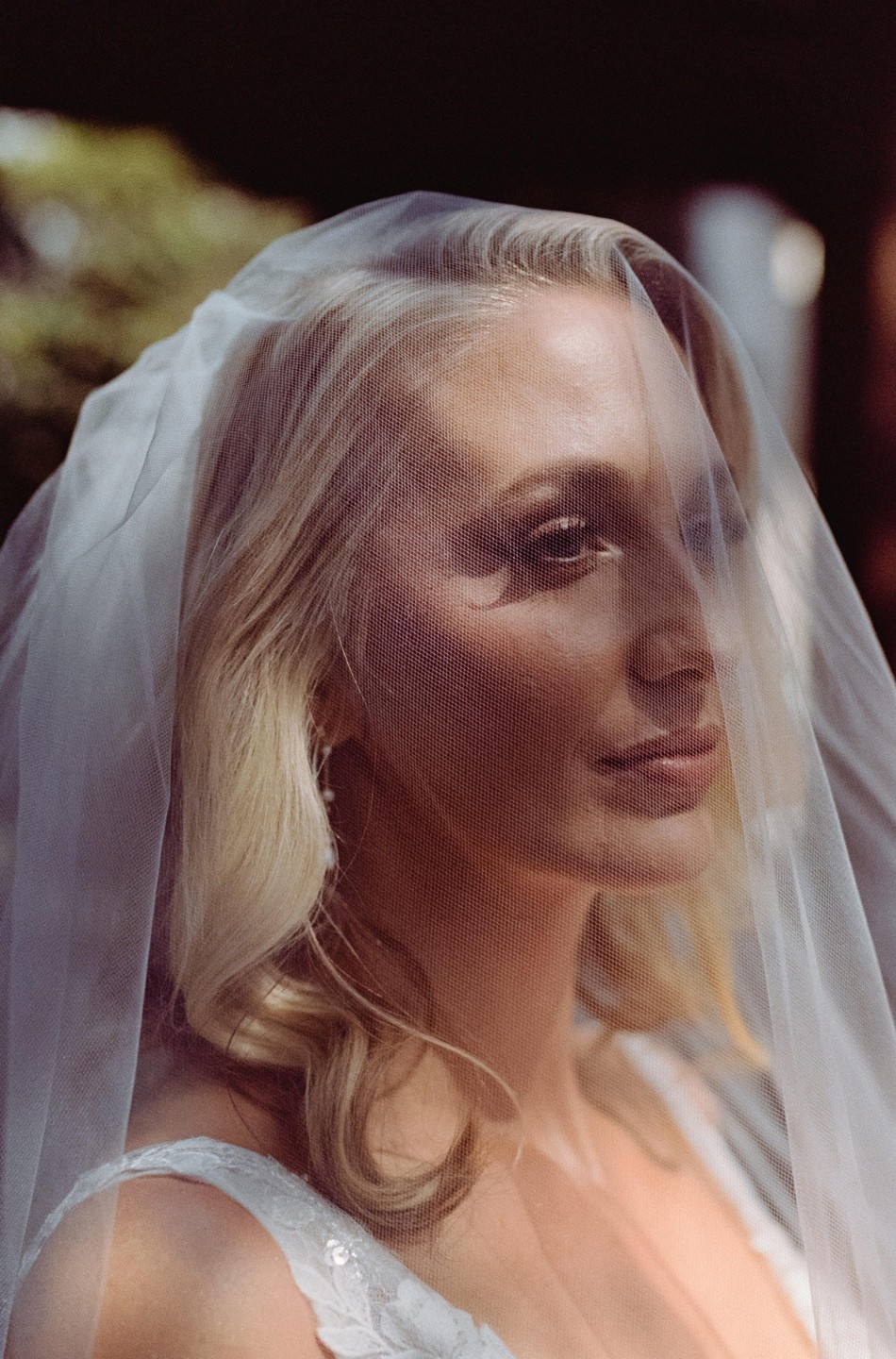 A woman with blonde hair is visible through a white veil covering her face.