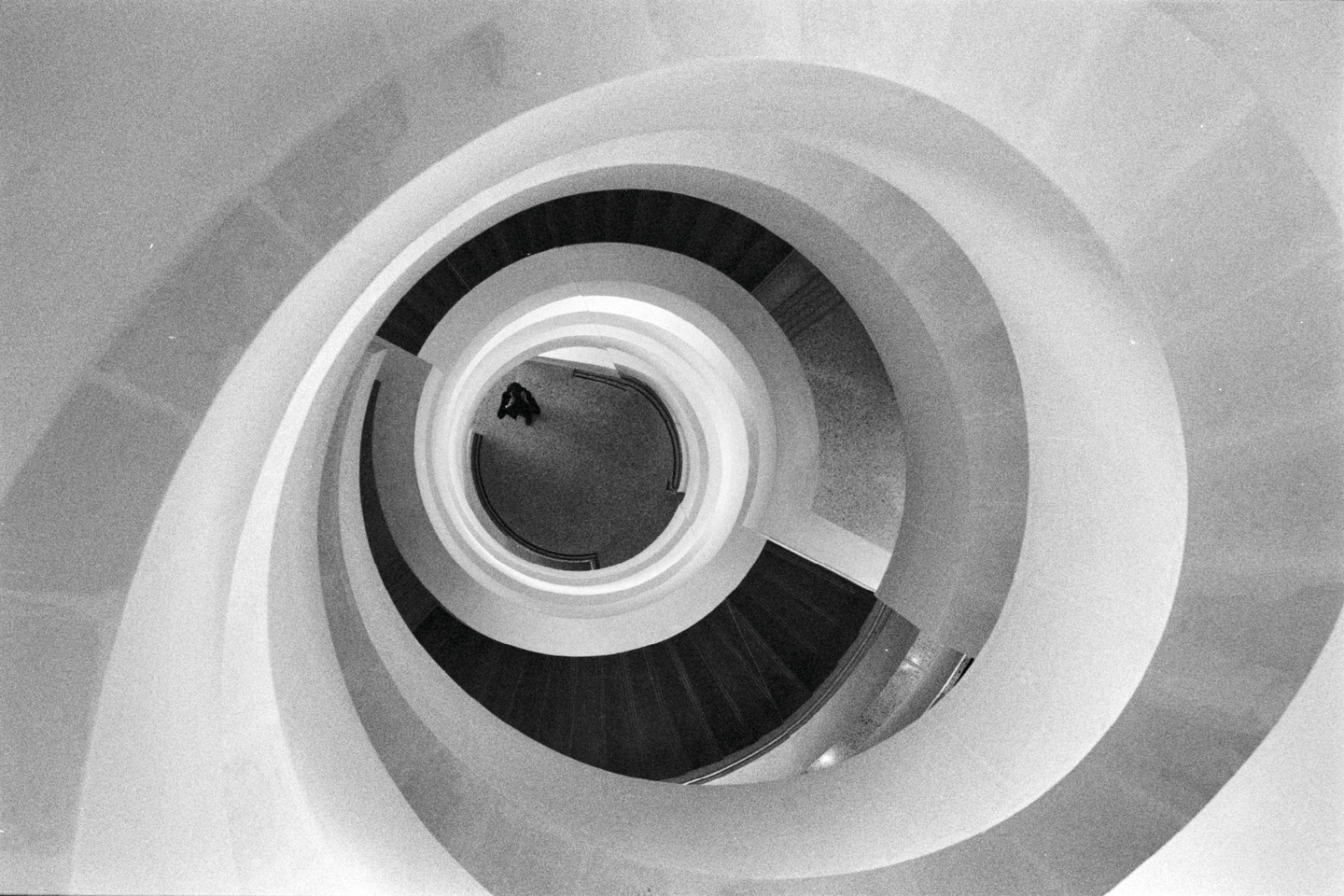 A person stands at the bottom of a spiral staircase in a modern building.