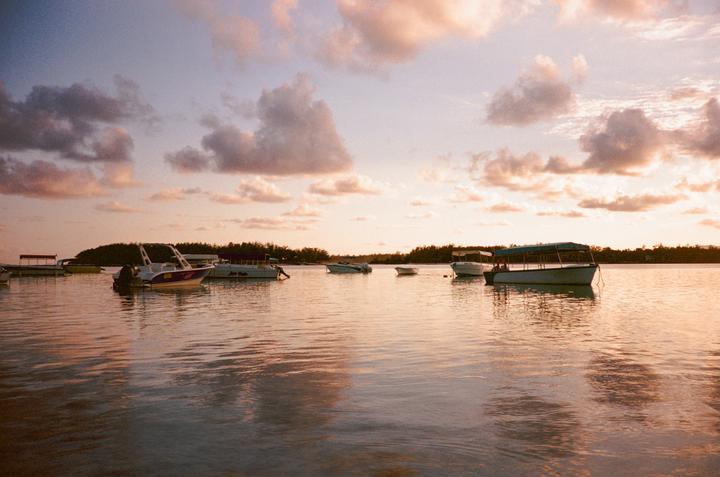 Several boats are moored on a body of water under a cloudy sky at sunset.