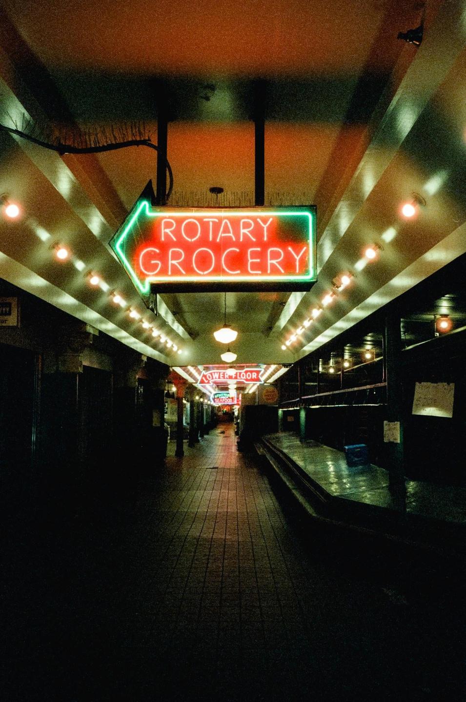A neon sign for "Rotary Grocery" points down a long, empty hallway lined with lights.