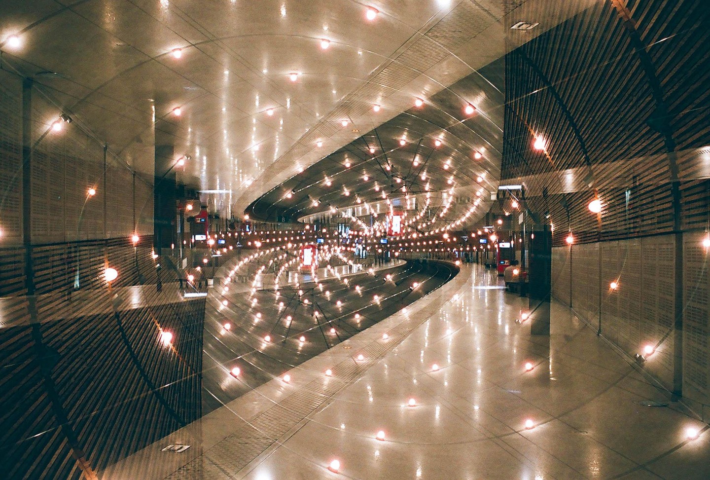 A double exposure shows the interior of a train station with many lights reflecting on the floor and ceiling.