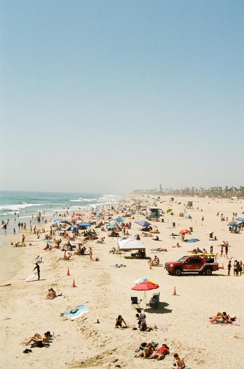 A crowded beach is filled with people swimming, sunbathing, and relaxing under colorful umbrellas and tents.